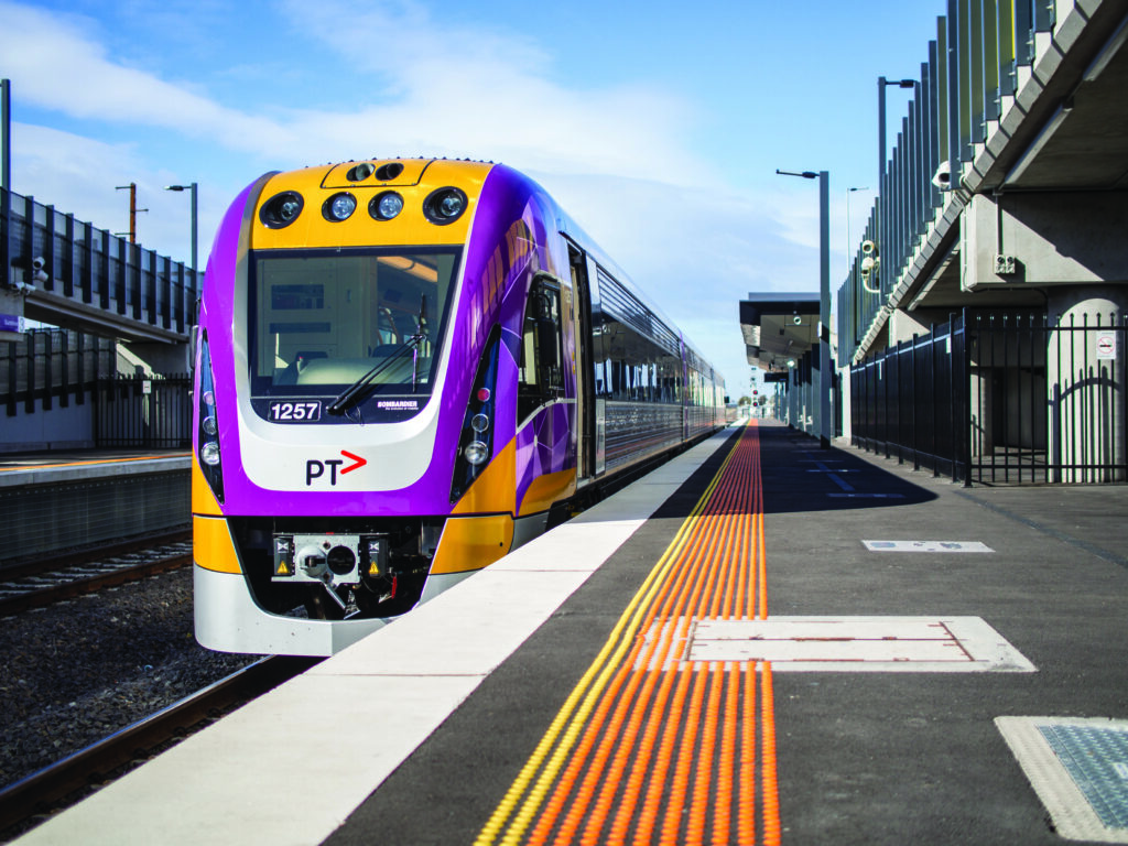 Working to provide exceptional service to the public, V/Line employs a dedicated workforce of more than 2,100 people, including many who live and work in regional Victoria. - A purple train sits at an empty train station, there are no people, the sun is shining