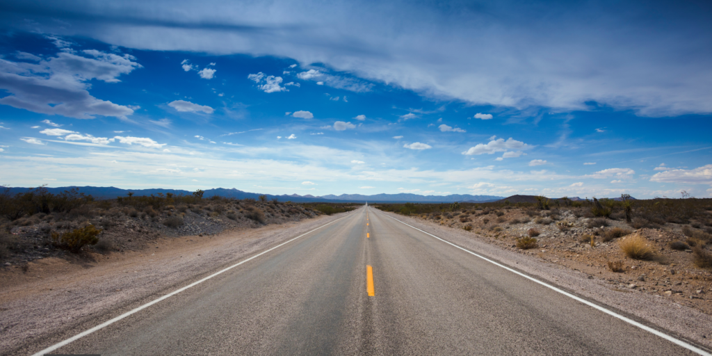 an image of an open highway in the desert. the sky is blue and the road markings are yellow